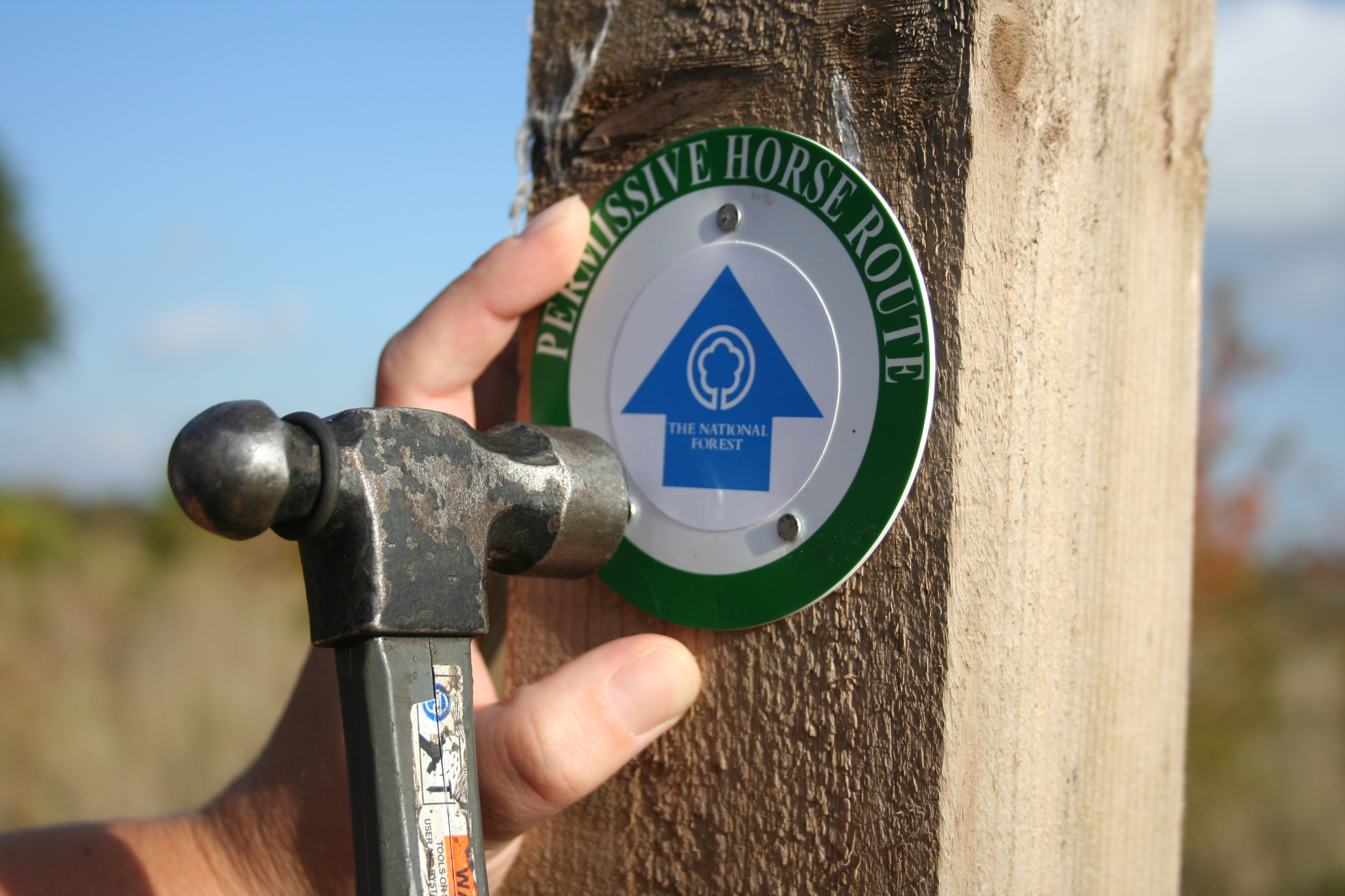 A close up of a waymarker being installed on a post with a hammer and nails.